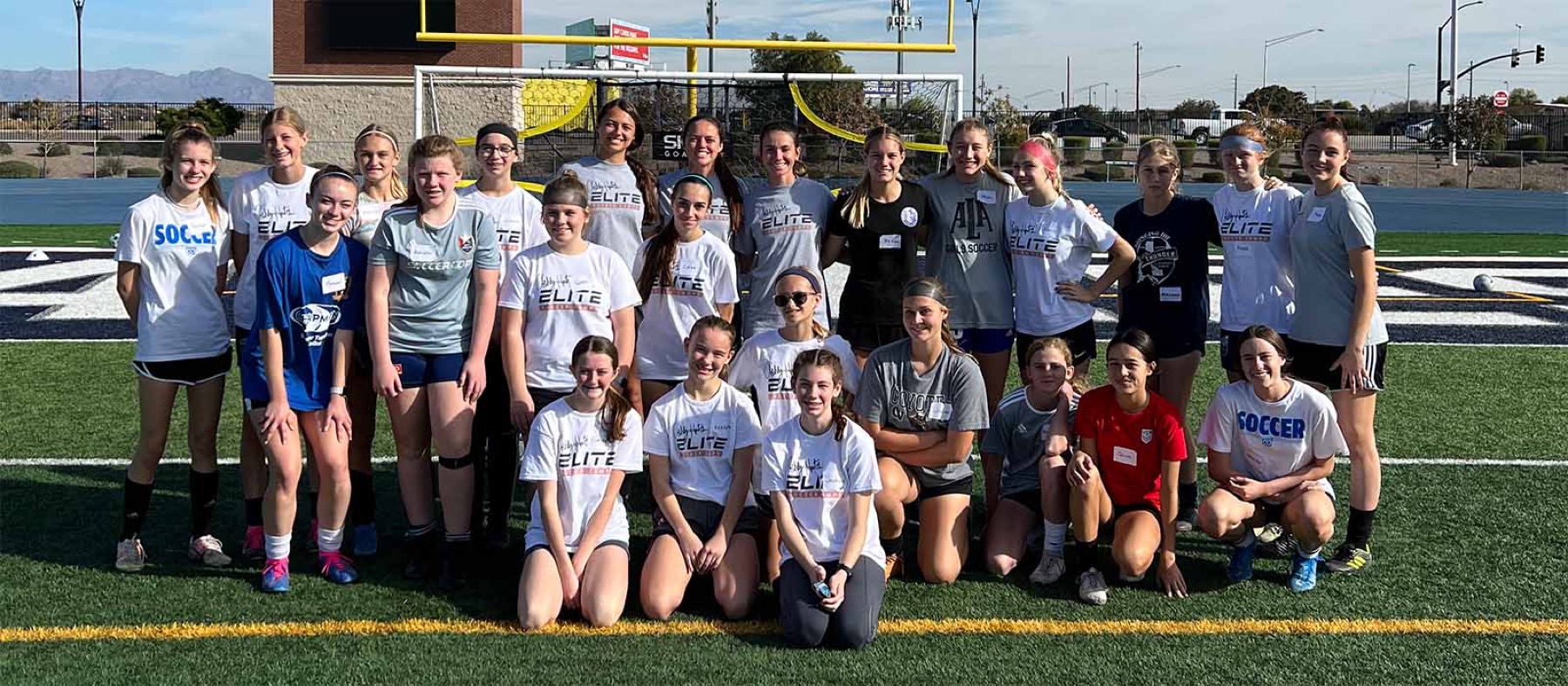 A large group of young players lined up on a turf field at an Ashley Hatch Elite camp.