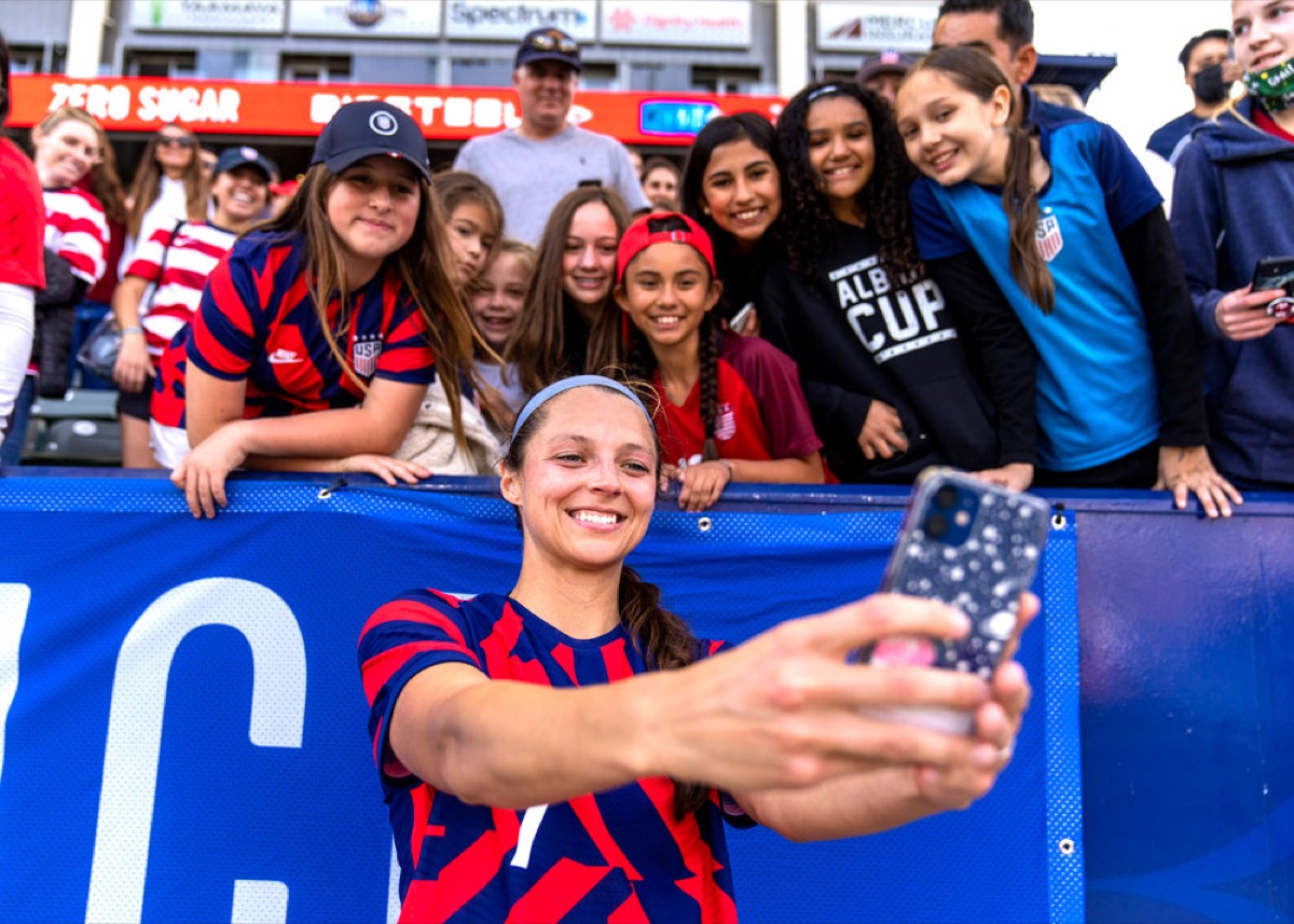 Ashley Hatch taking a selfie with a group of young players leaning over the barrier after a match.